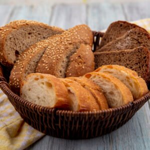 side view of breads as sliced seeded brown cob rye and crusty ones in basket on plaid cloth on wooden background