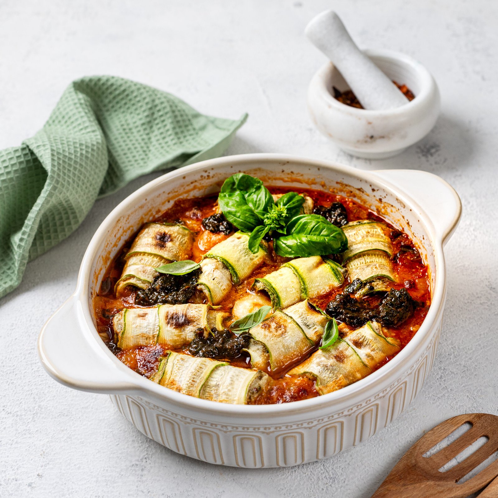 italian zucchini rolls with cream cheese filling, baked in tomato sauce on a white background.