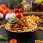 spaghetti saute in a gray plate with tomatoes and basil